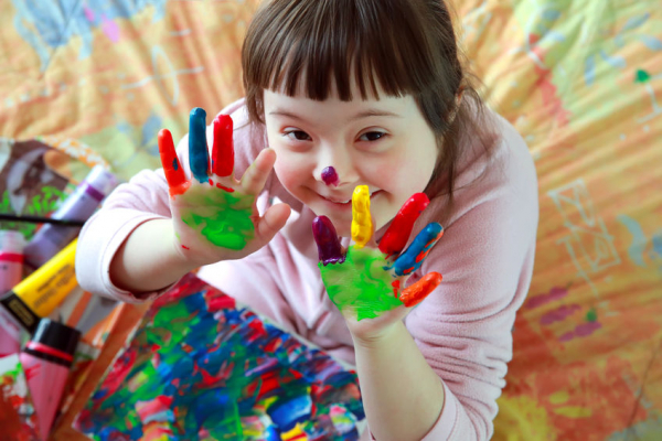 Muestra otra lado de la discapacidad, al ver una niña con Síndrome de Down con las manos pintadas de colores, disfrutando de la experiencia con una amplia sonrisa