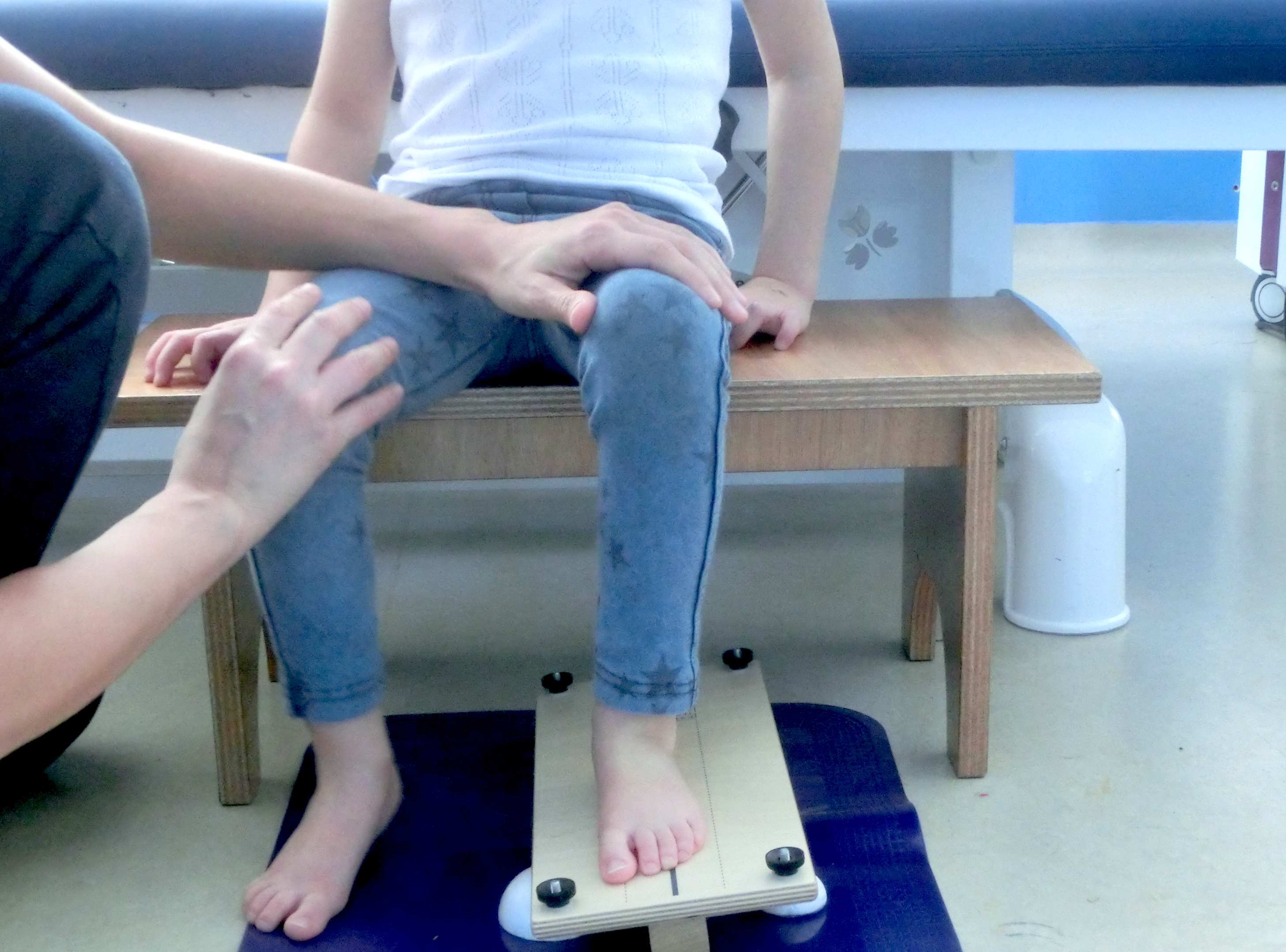 una niña está realizando una sesión de Perfetti con su pie izquierdo sobre una tabla que se inclina lateralmente