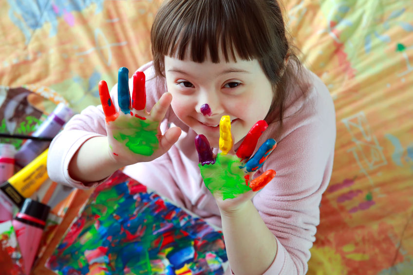 Niña con Síndrome de Down con las manos pintadas de colores